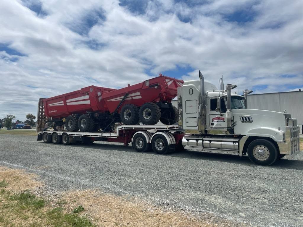 White Semi Truck Hauling a Red Lowboy Trailer with Heavy Machinery — Rainbow and Sons Heavy Haulage in Wells Crossing, NSW