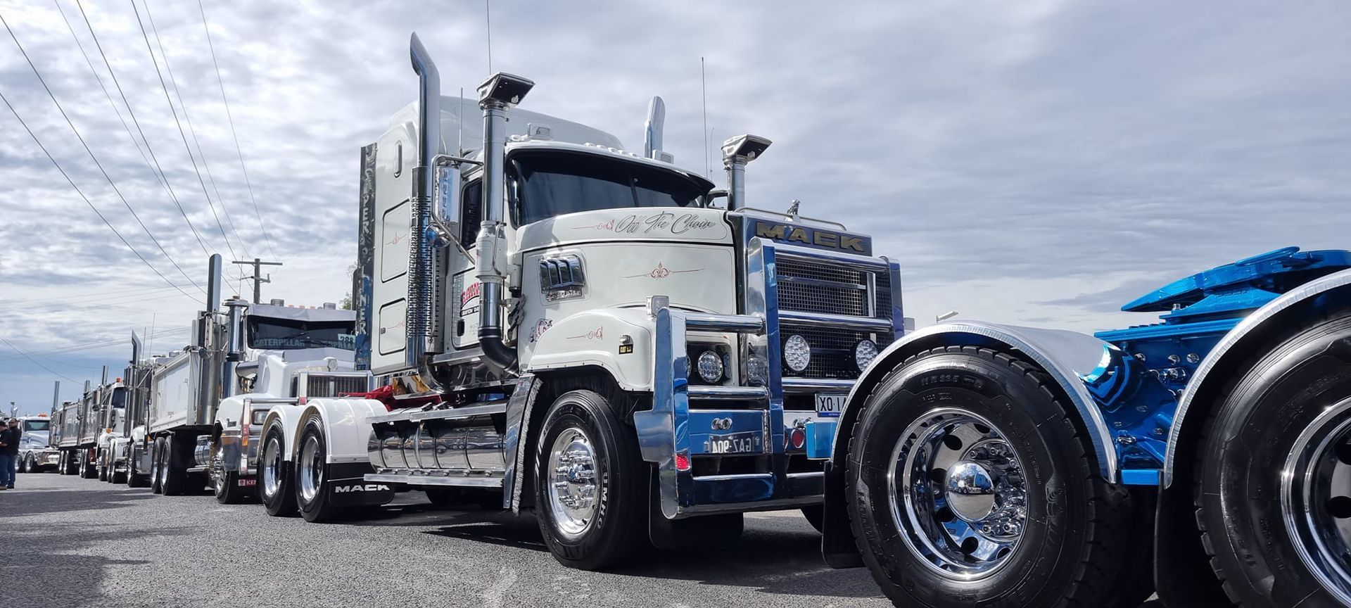White and Blue Semi Trucks Lined up In a Parade on A Wet City Street — Rainbow and Sons Heavy Haulage in Coffs Harbour, NSW