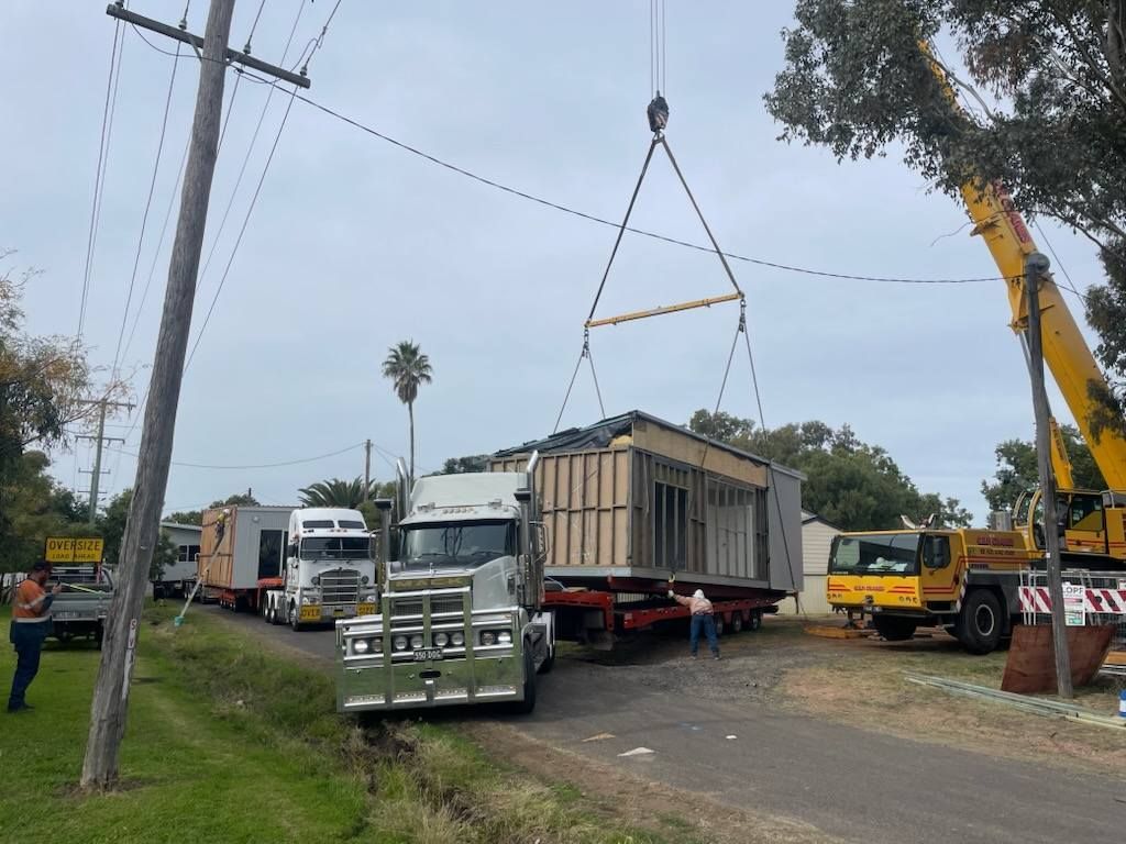 Crane Lifting a Small Building onto A Truck at A Roadside Work Site — Rainbow and Sons Heavy Haulage in Wells Crossing, NSW