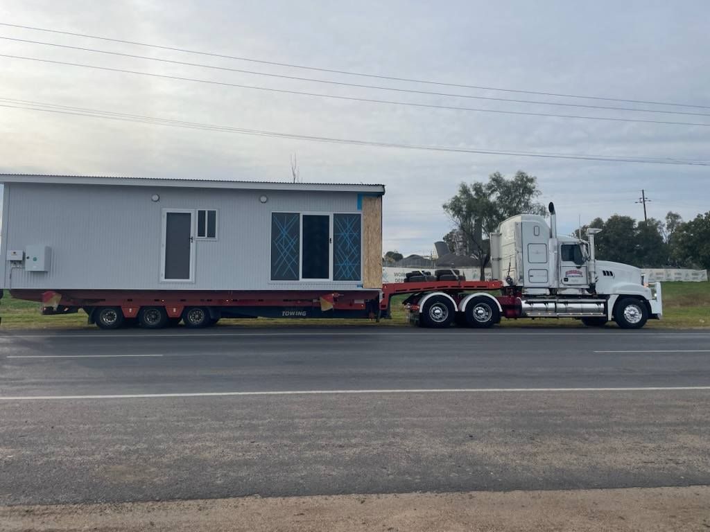 White Semi Truck Hauling a Grey Modular Home on A Highway — Rainbow and Sons Heavy Haulage in Wells Crossing, NSW