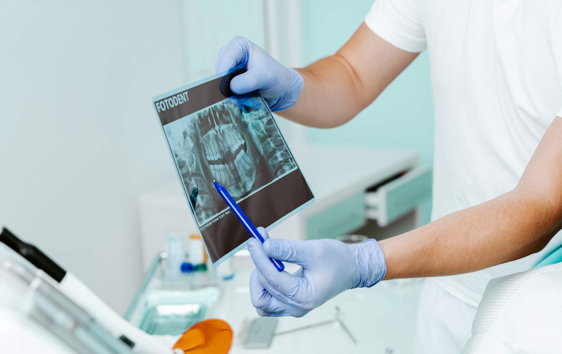 Doctor in blue gloves reviewing an X-ray and pointing with a pen in a clinic Doctor in blue gloves reviewing an X-ray and pointing with a pen in a clinic