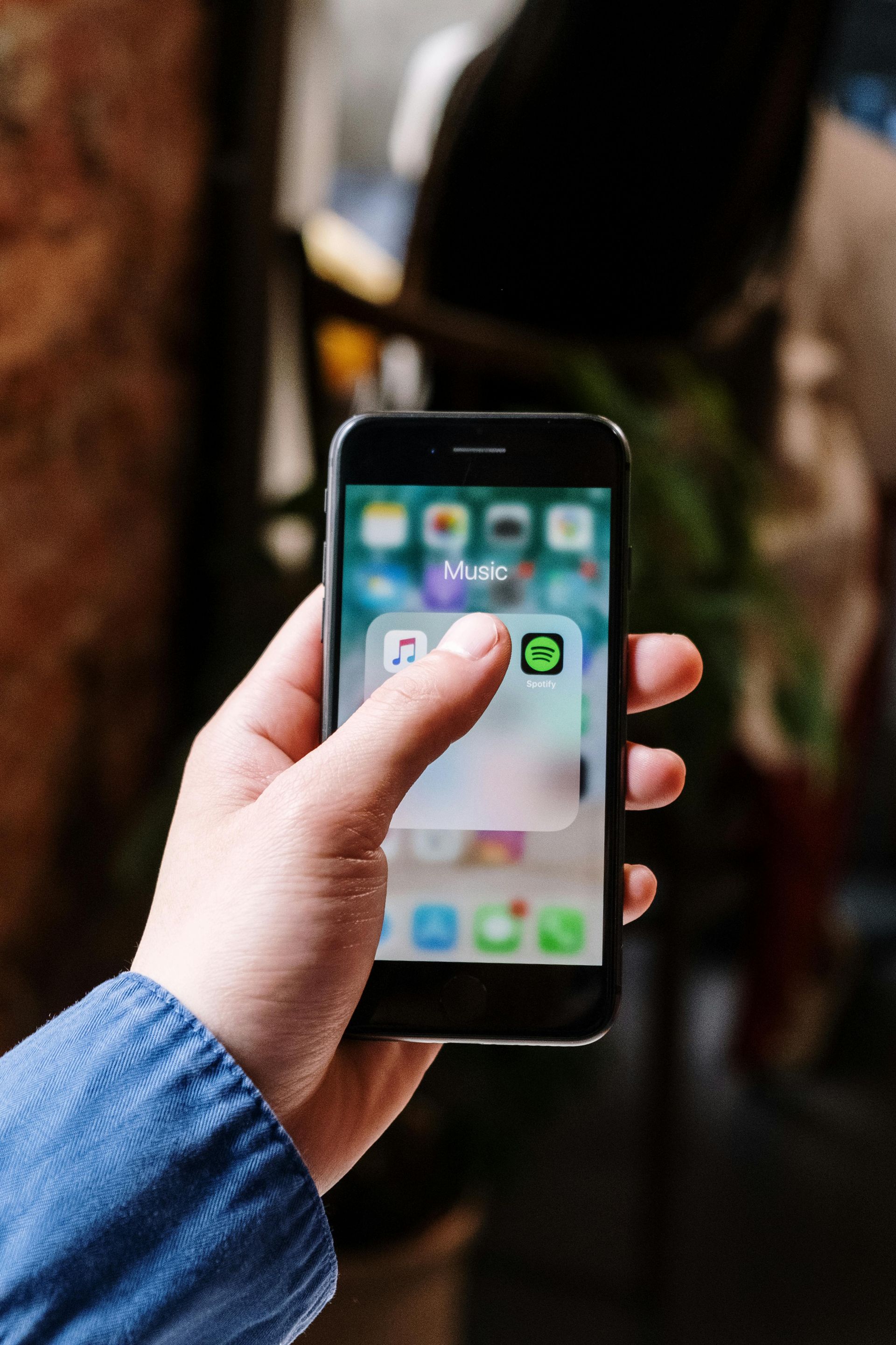 Hand holding a smartphone, tapping the Spotify app icon on the screen.
