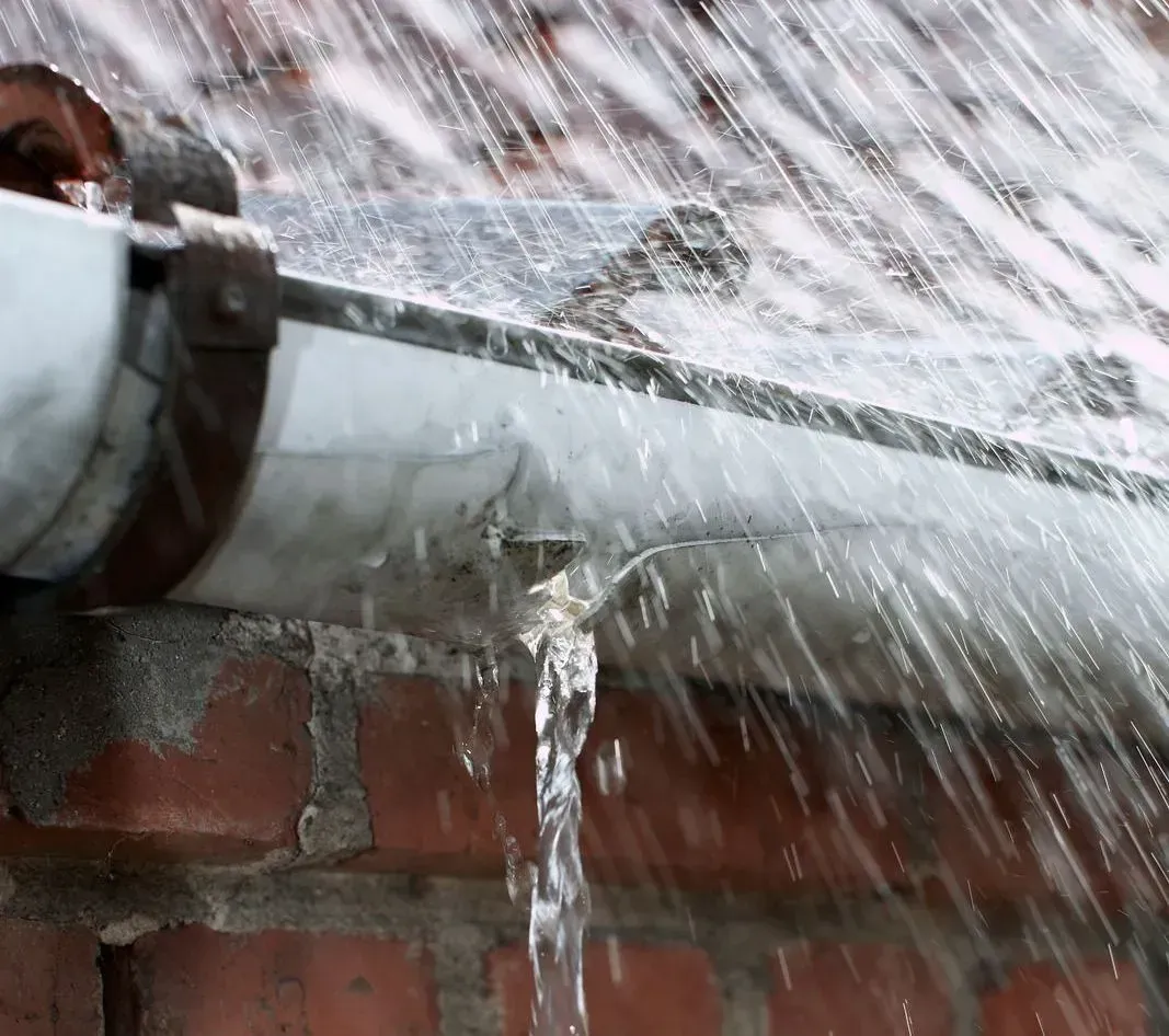 Water spraying from a hose onto a brick wall and gutter during rain cleaning.