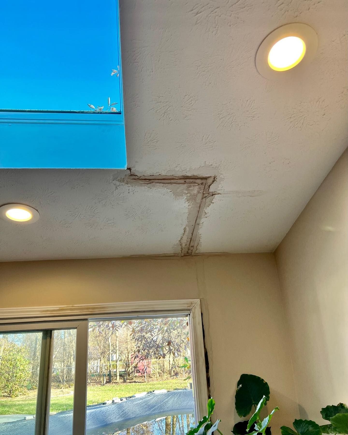 Ceiling with water damage and blue tarp covering an opening above a room window