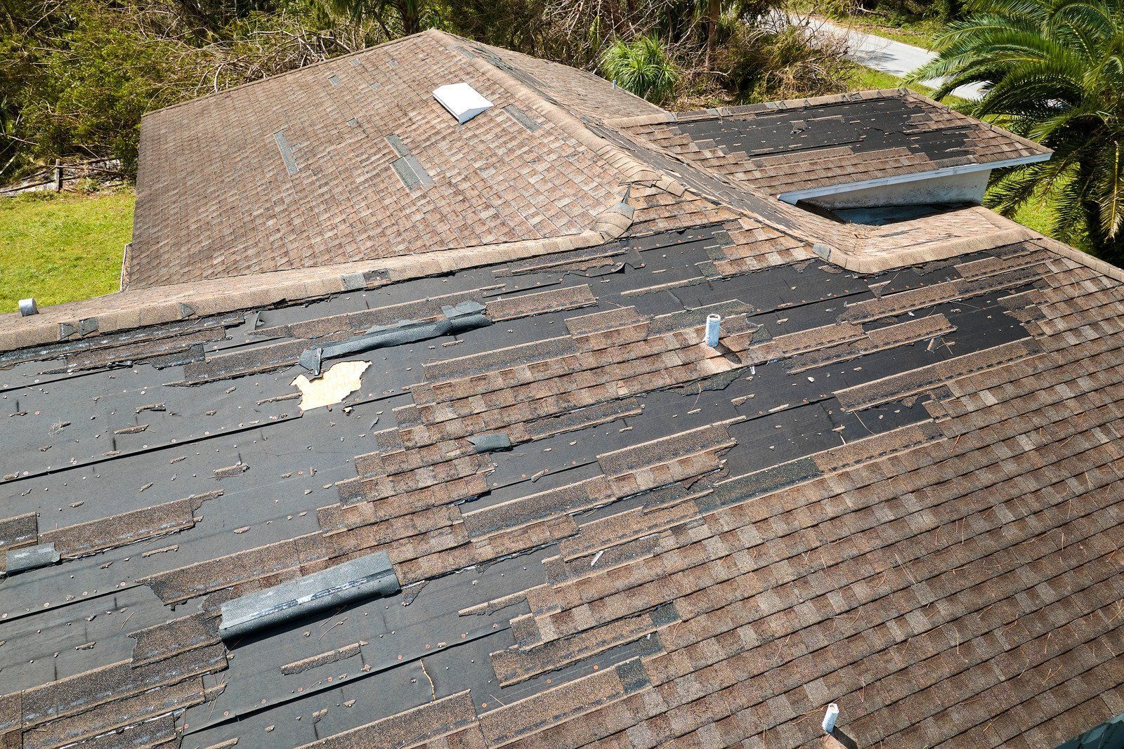Damaged asphalt shingle roof with missing shingles and exposed underlayment.