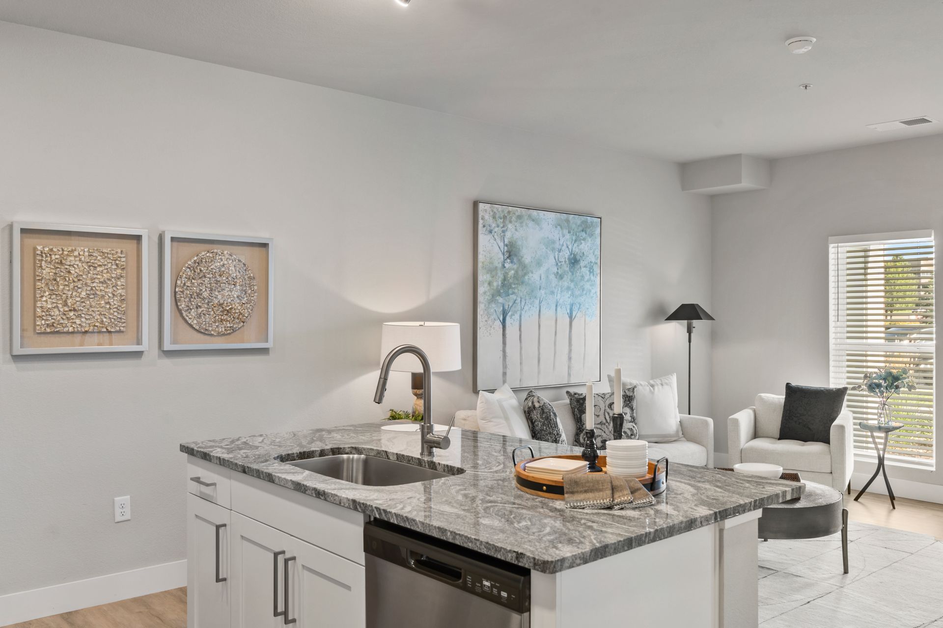 Bright modern kitchen with a granite island opening to a gray living area and large window.