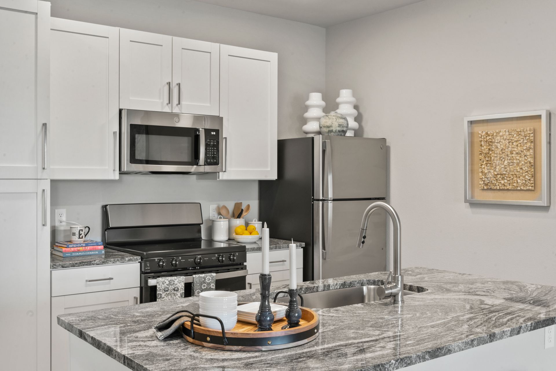 Modern kitchen with white cabinets, stainless appliances, granite island, and decorative tray centerpiece