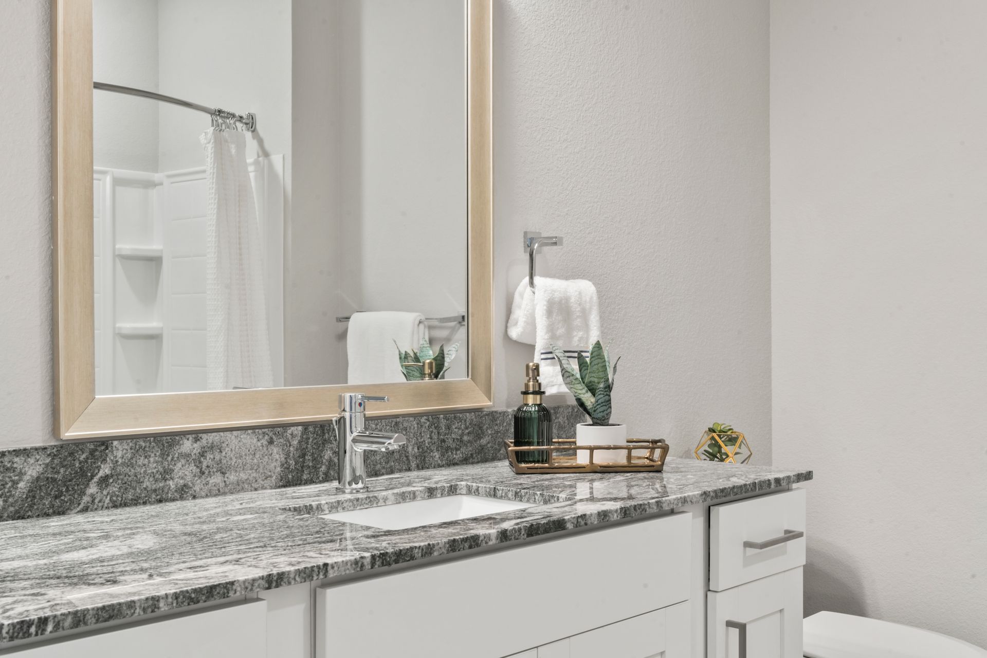 Bathroom vanity with gray marble countertop, mirror, and small decorative items