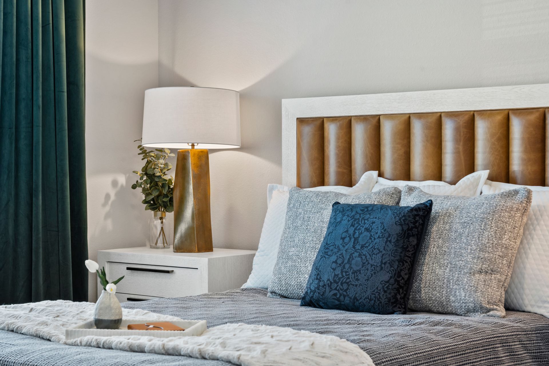 Cozy bedroom with blue pillows, tufted headboard, bedside lamp, and soft gray bedding