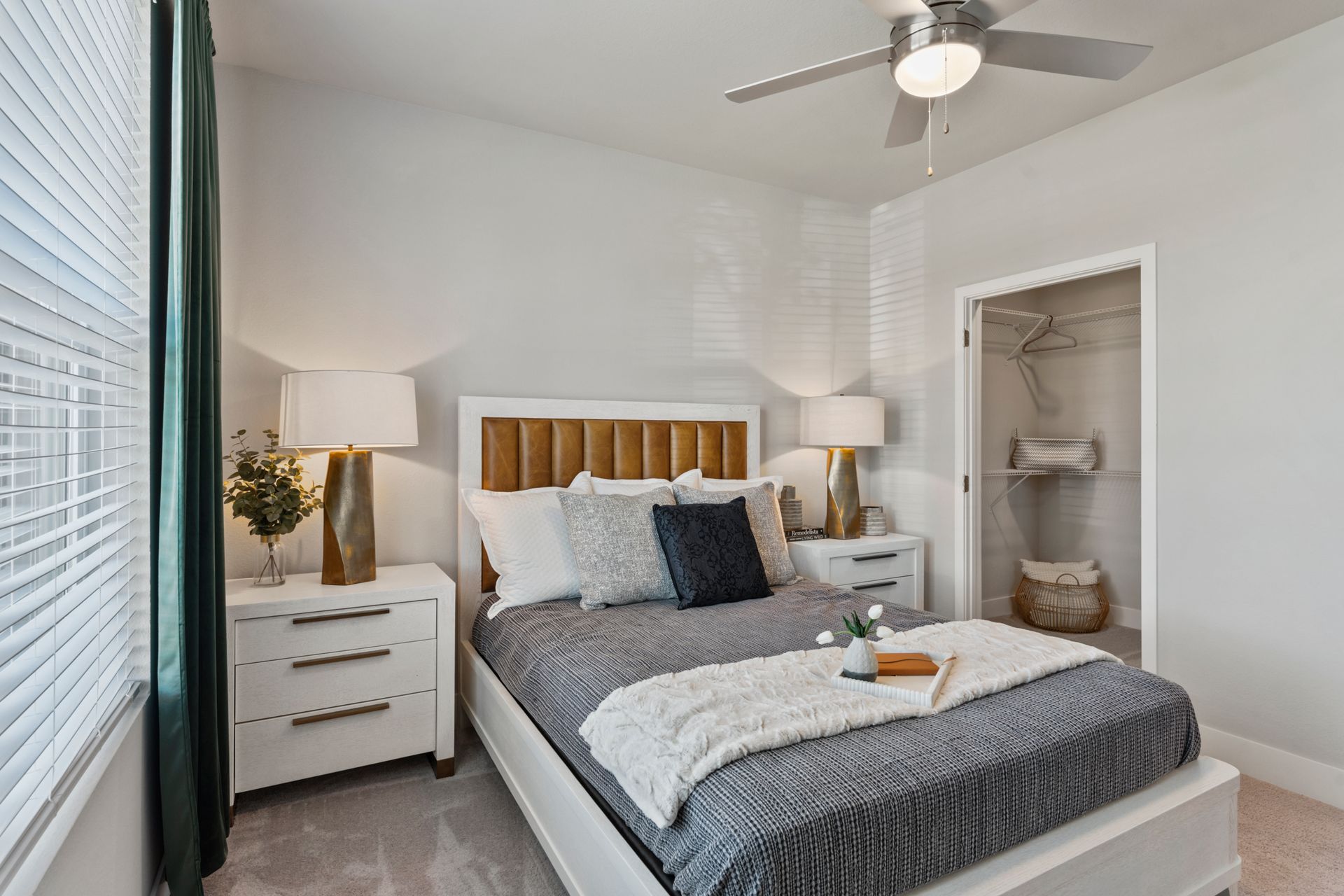 Bright bedroom with a bed, nightstands, lamps, ceiling fan, and an open closet alcove.
