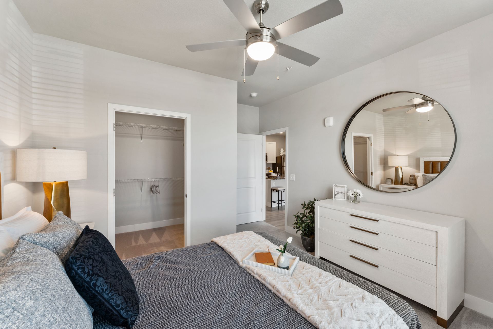 Bright bedroom with gray bedspread, white dresser, round mirror, and open closet door