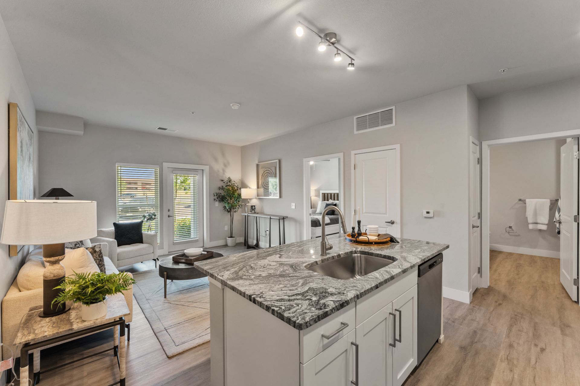 Bright open kitchen and living room with gray island, granite countertops, white walls, and sliding glass doors