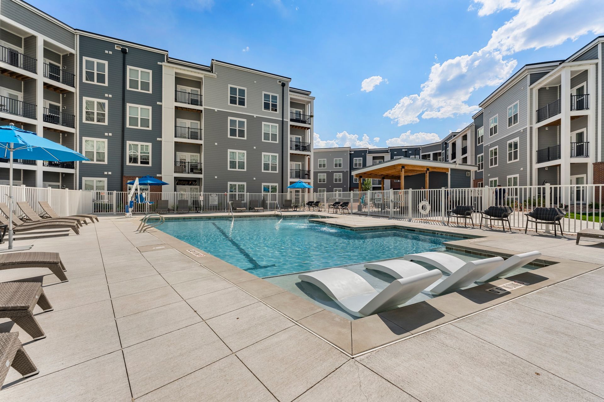 Outdoor apartment pool with lounge chairs and modern buildings on a sunny day