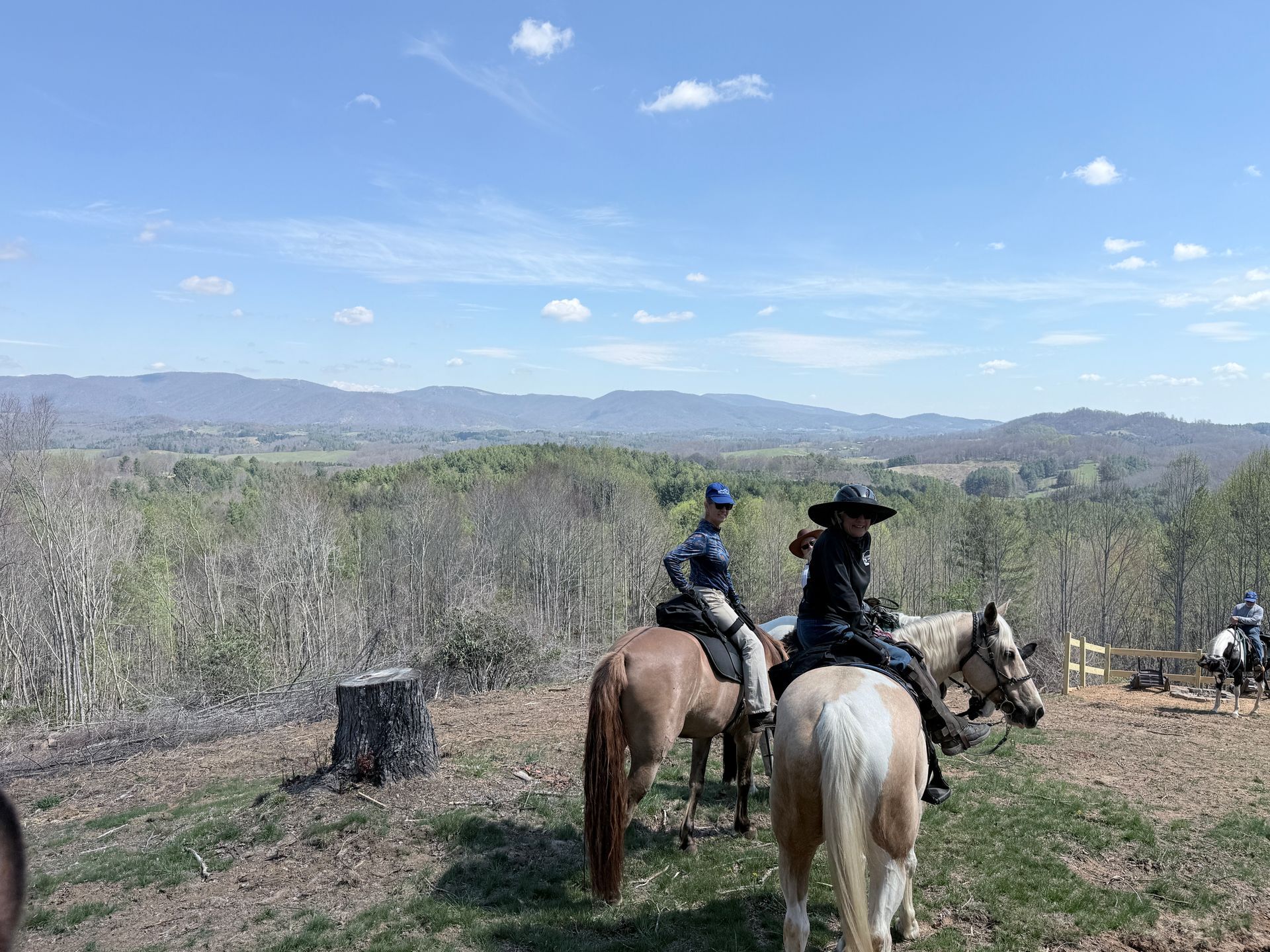 Two people on horseback overlooking a dry valley and distant mountains under a bright blue sky