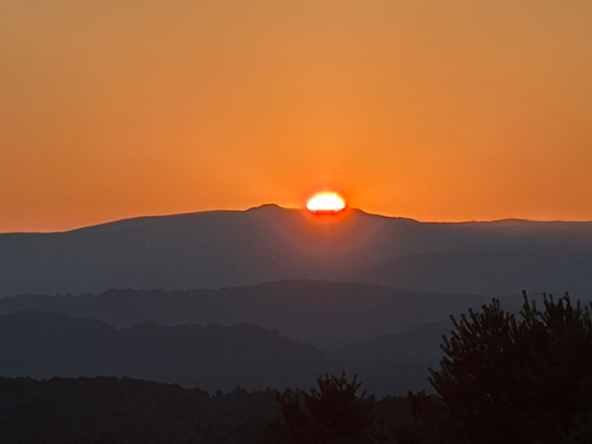 Sun setting behind dark mountain ridges under an orange sky