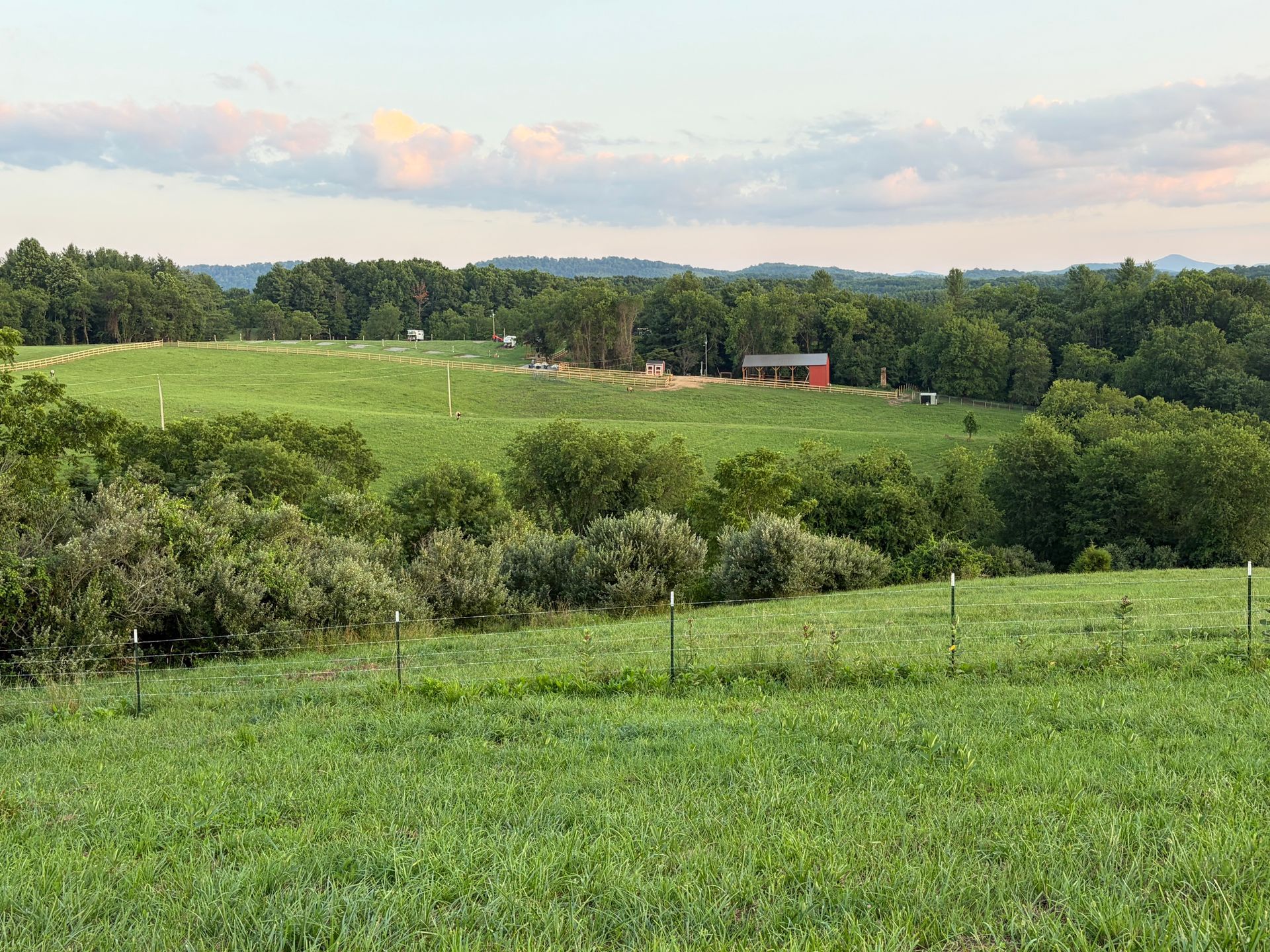 Rolling green pasture with trees and a small red barn under a cloudy sky