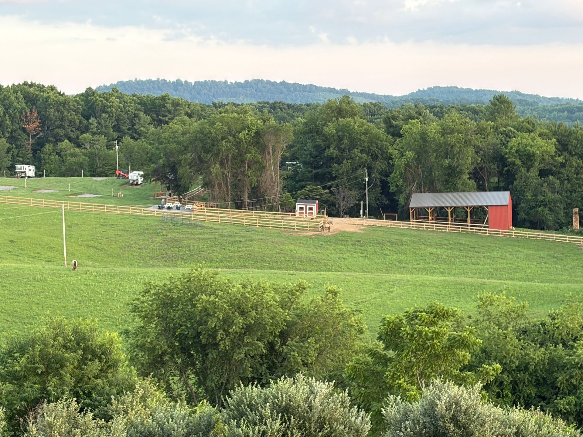 Green pasture with trees, hills, and a small barn under a cloudy sky