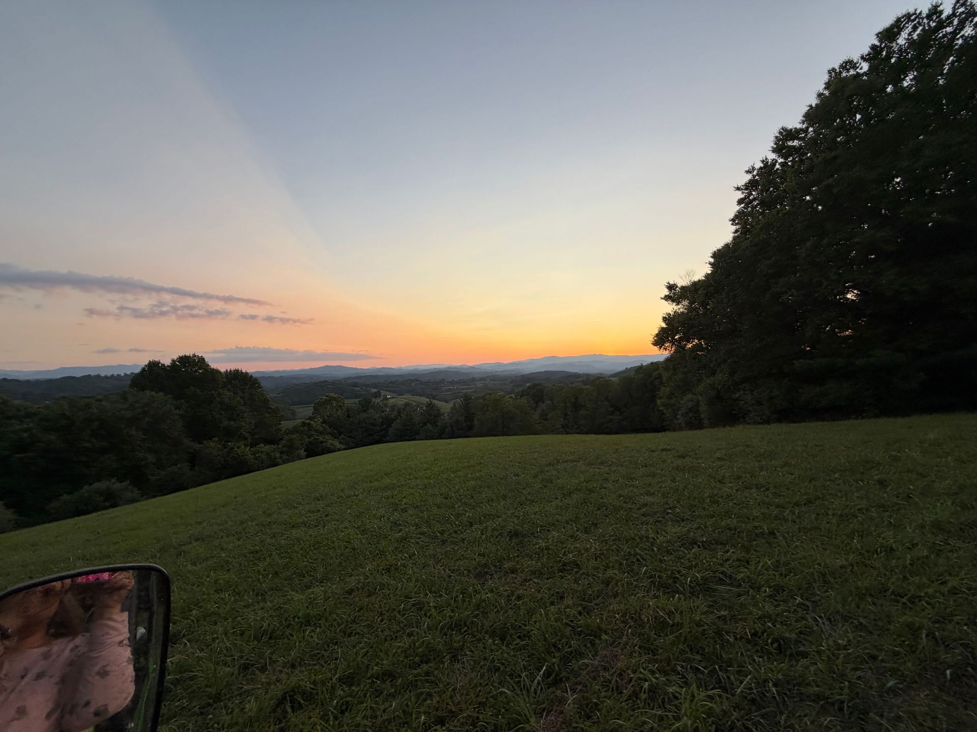 Sunset over a grassy hill with trees and distant mountains