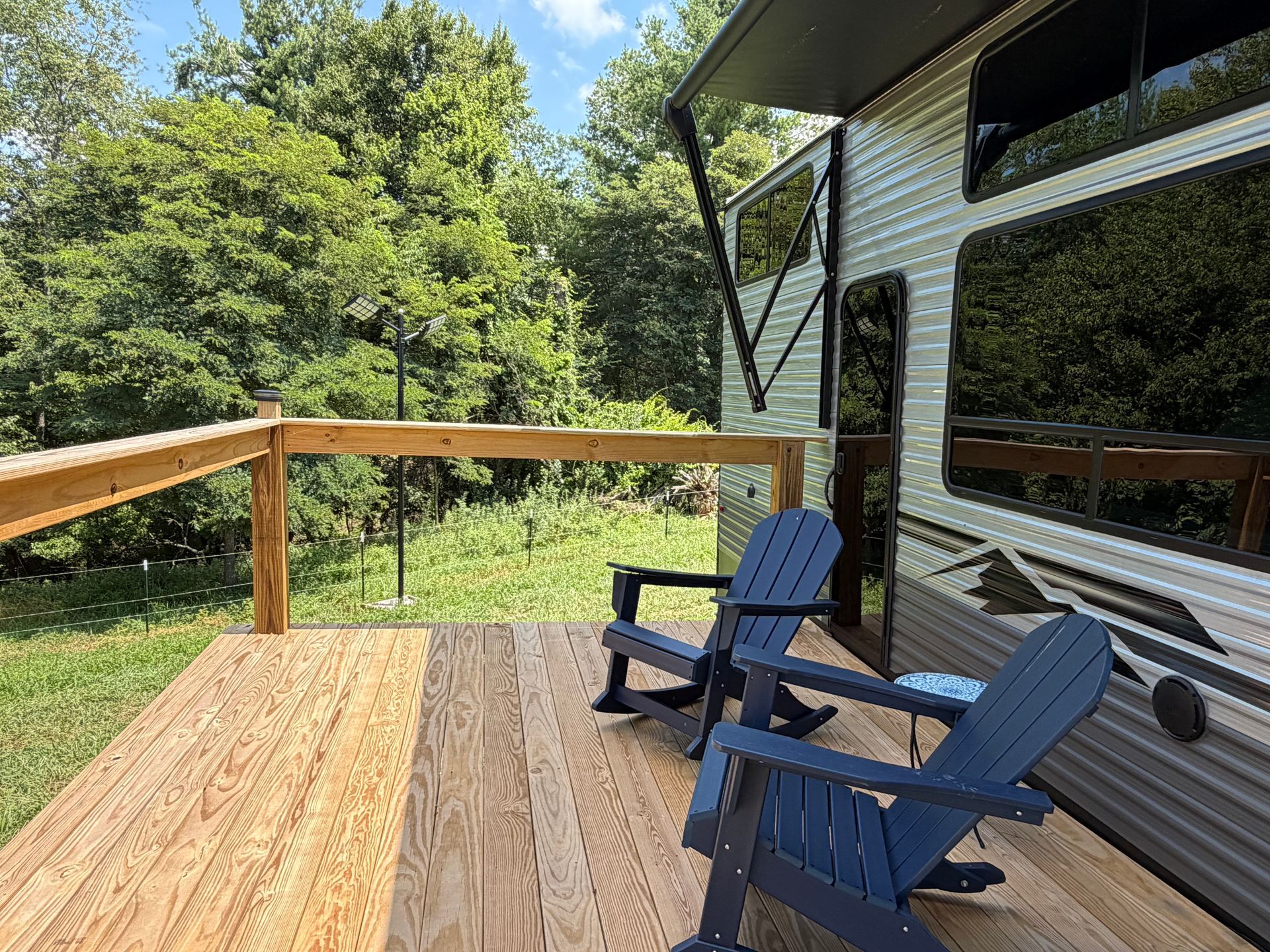 Wooden deck beside a house with two blue chairs overlooking a green wooded yard.