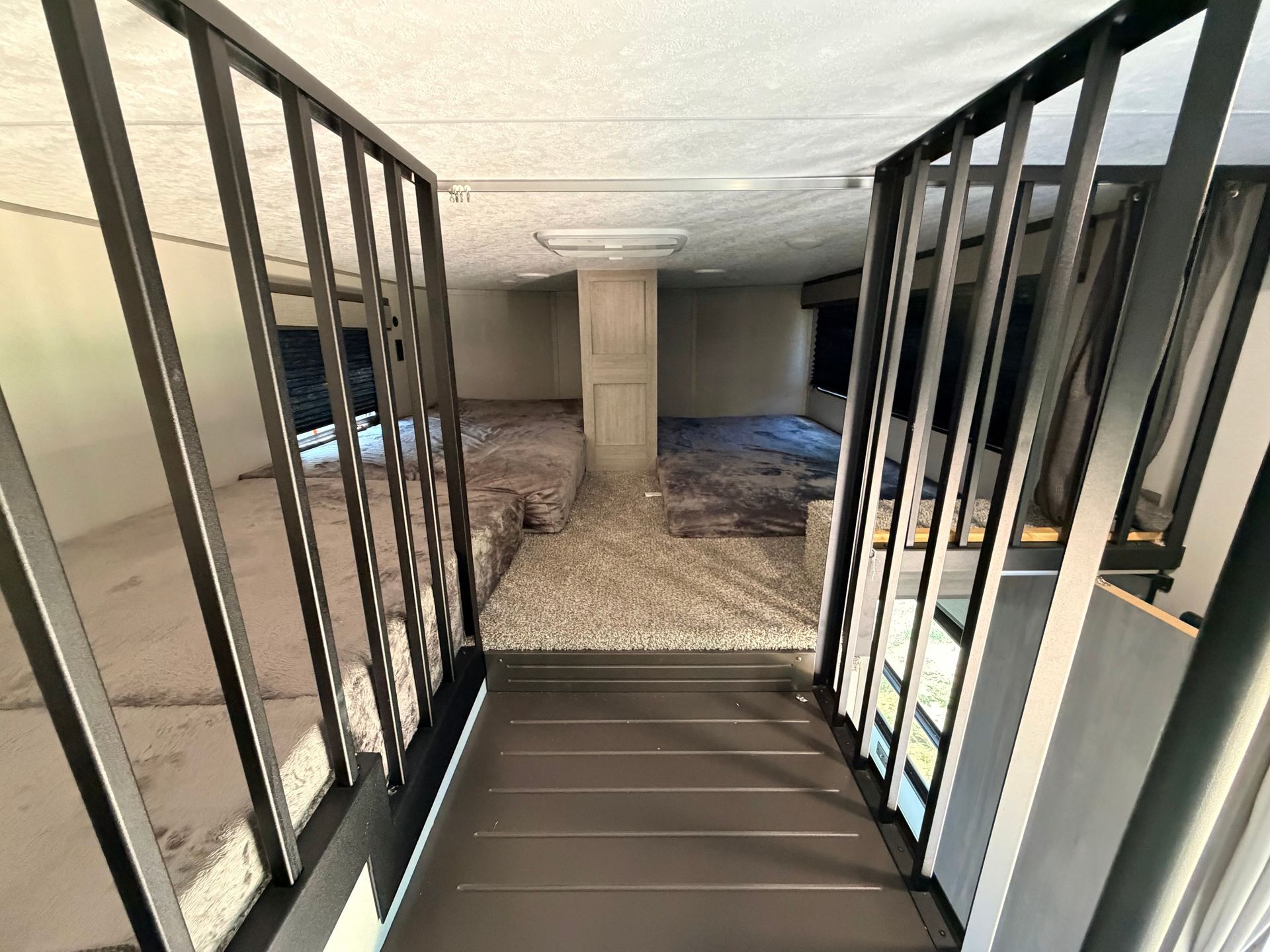 Interior view of a bunk room with black metal frames, carpeted floor, and multiple beds on both sides