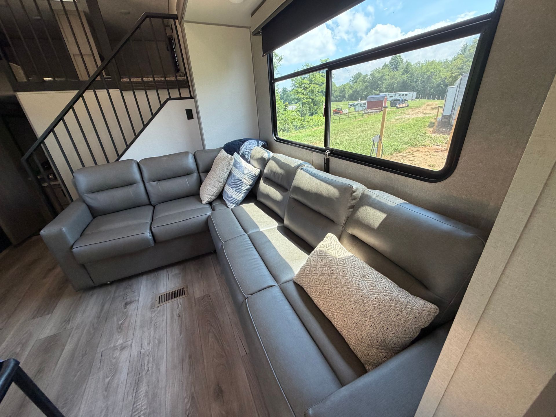 Modern living room with gray sectional sofa, large window, and staircase.