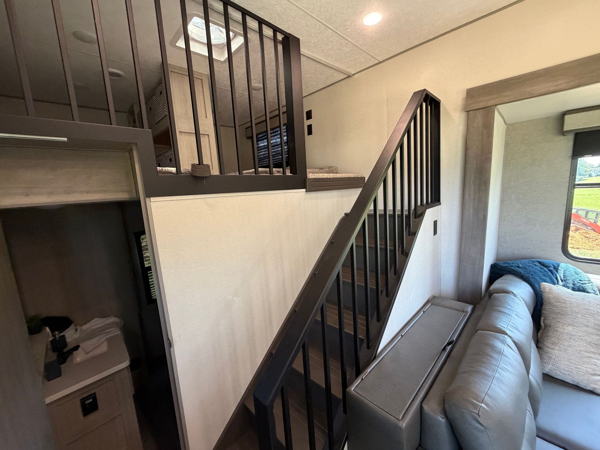 Small loft-style interior with black railing, white paneled wall, gray couch, and window light.