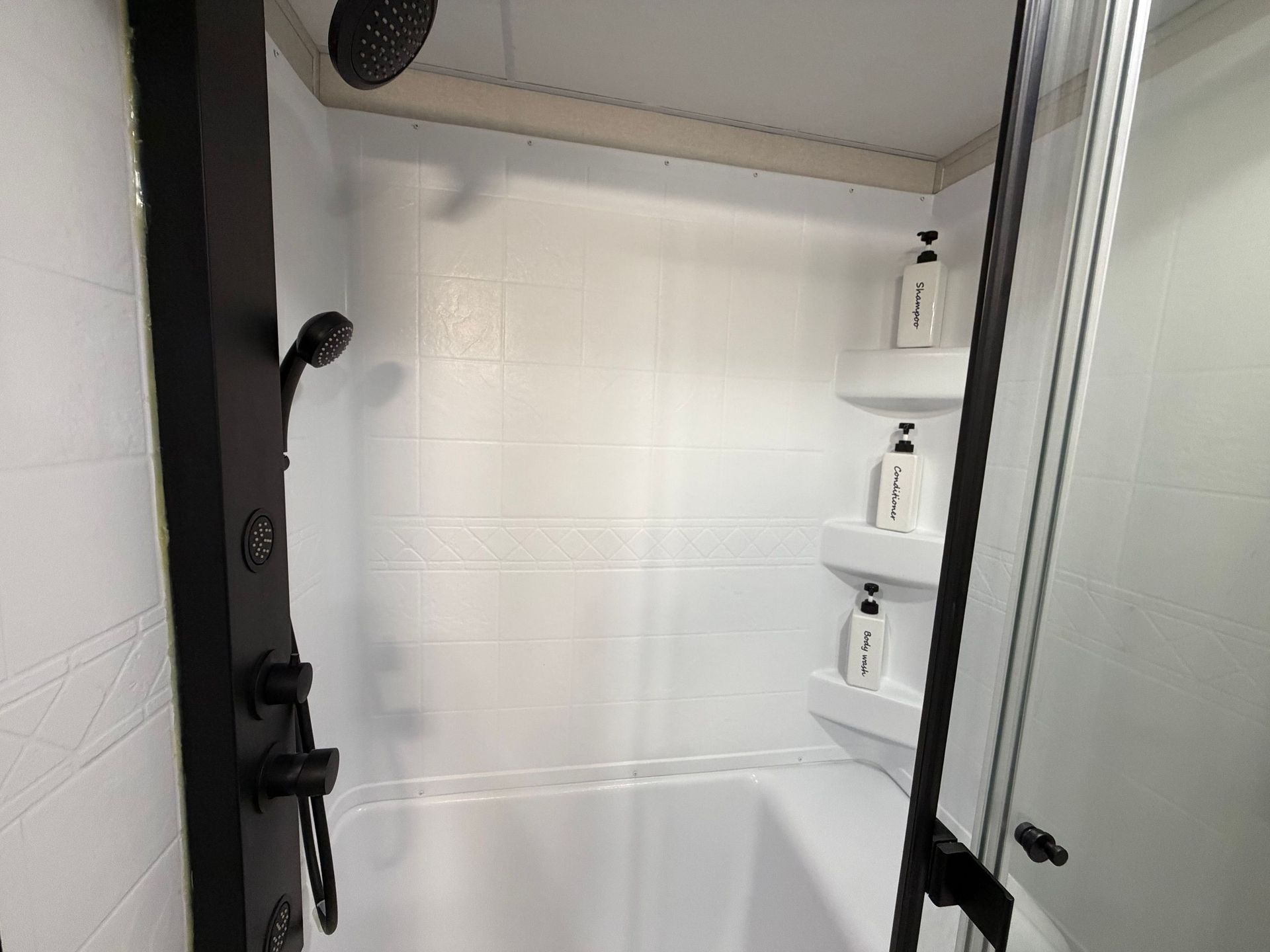 Small white tiled shower with glass door and built-in corner shelves for toiletries