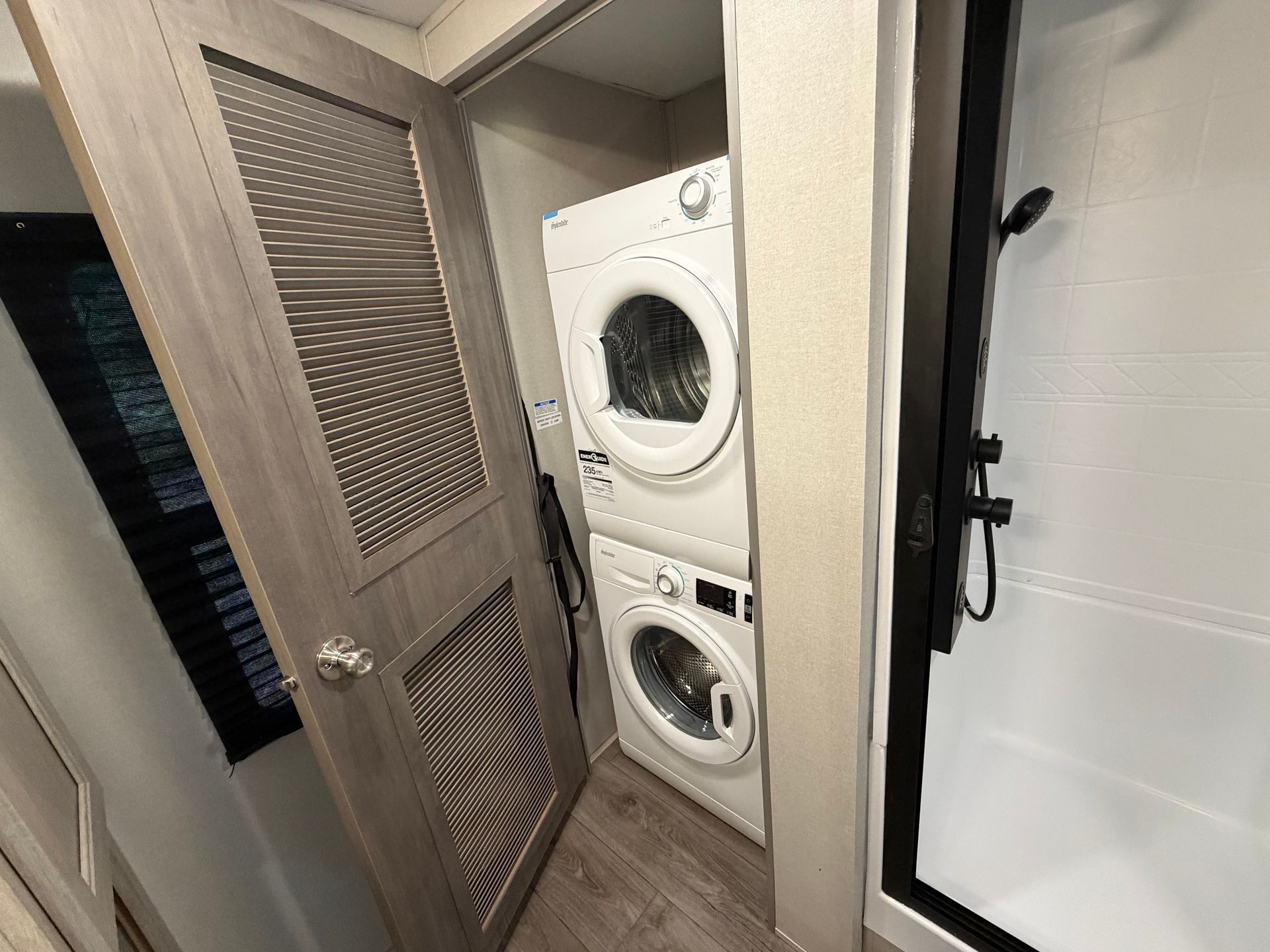 Stacked washer and dryer in a narrow laundry closet with louvered door and tiled floor