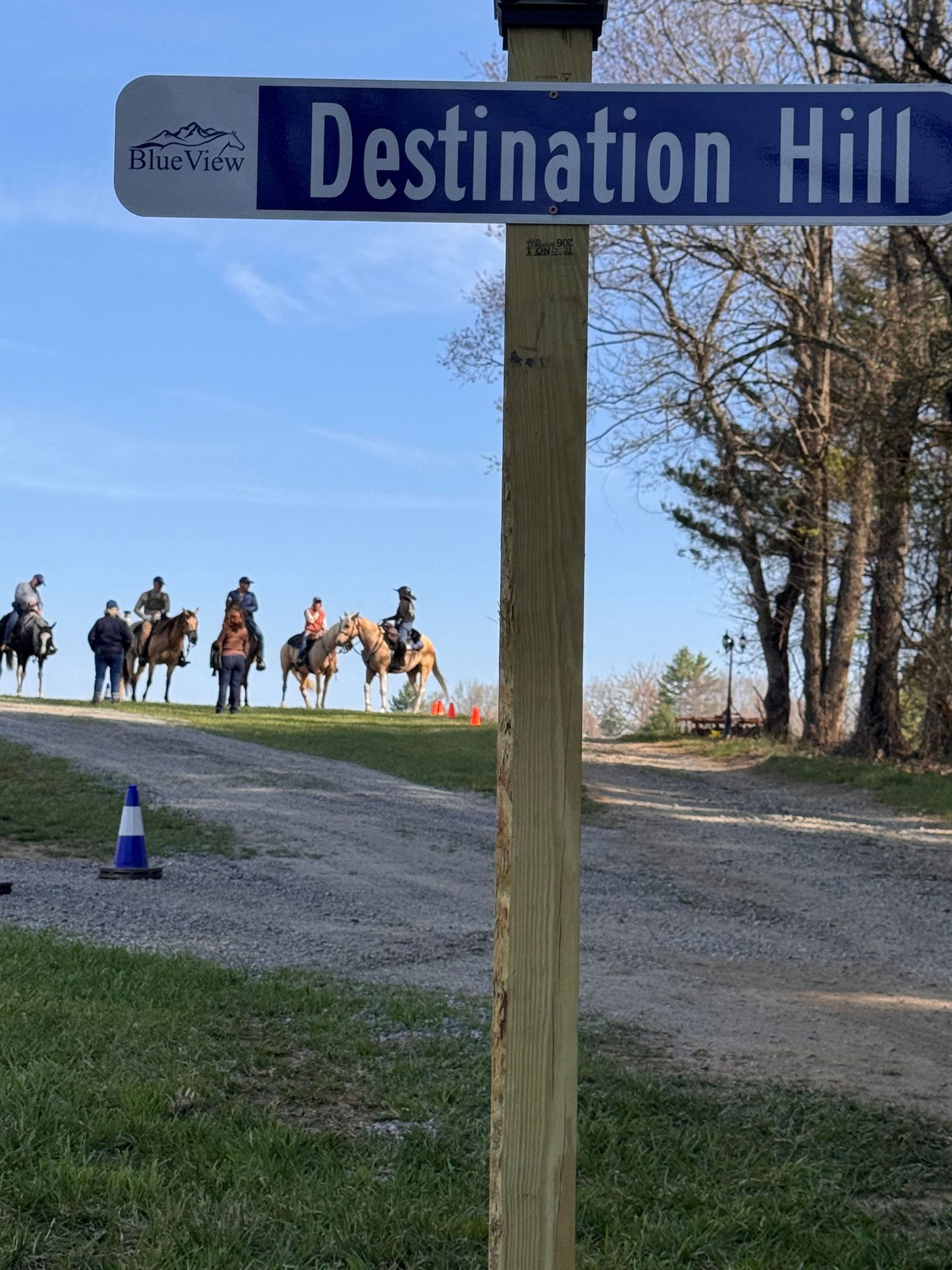 Trail sign reading “Destination Hill” with riders on horseback in the background.