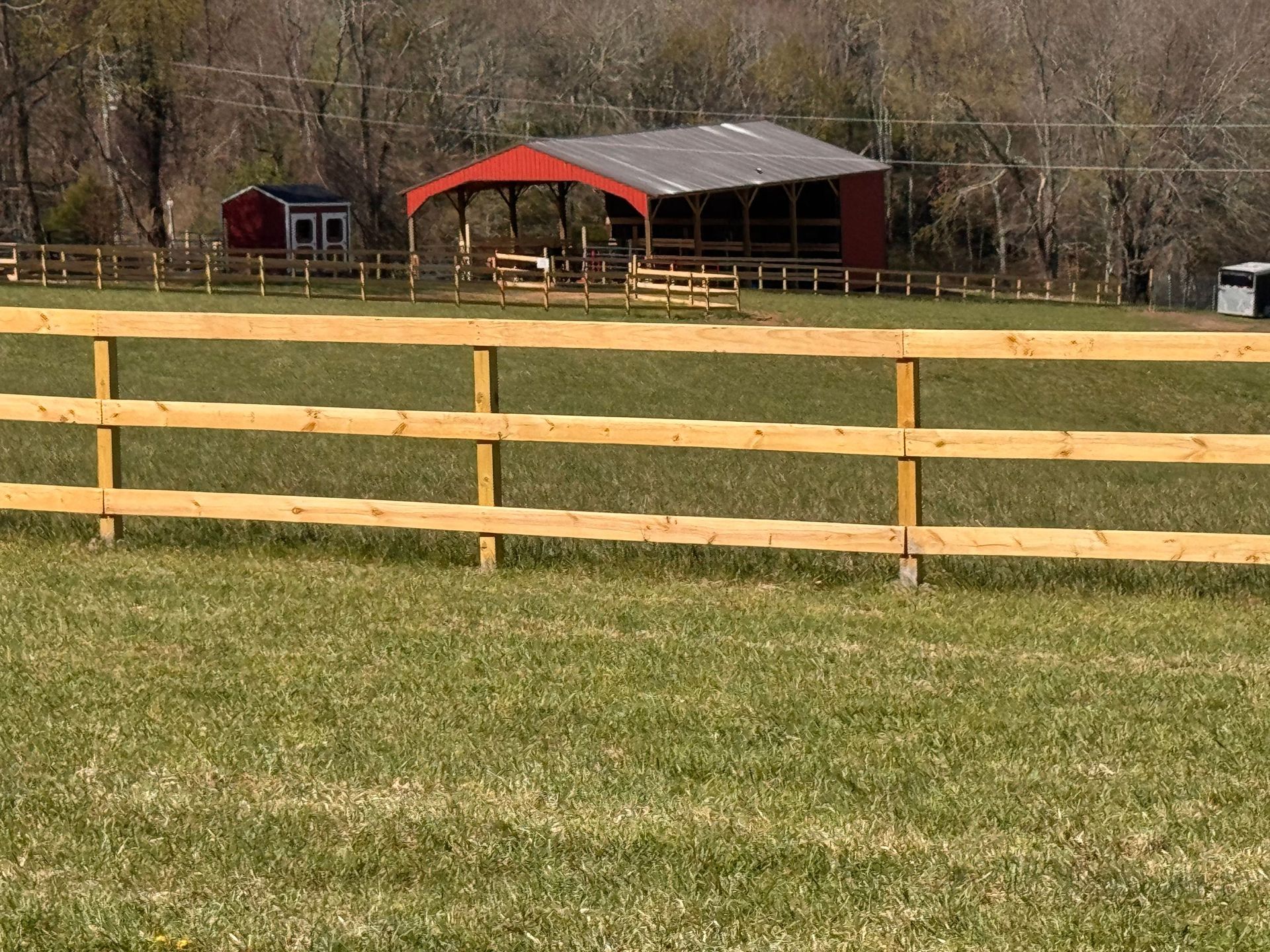Wooden fence in a grassy field with red barn-like structures and trees in the background