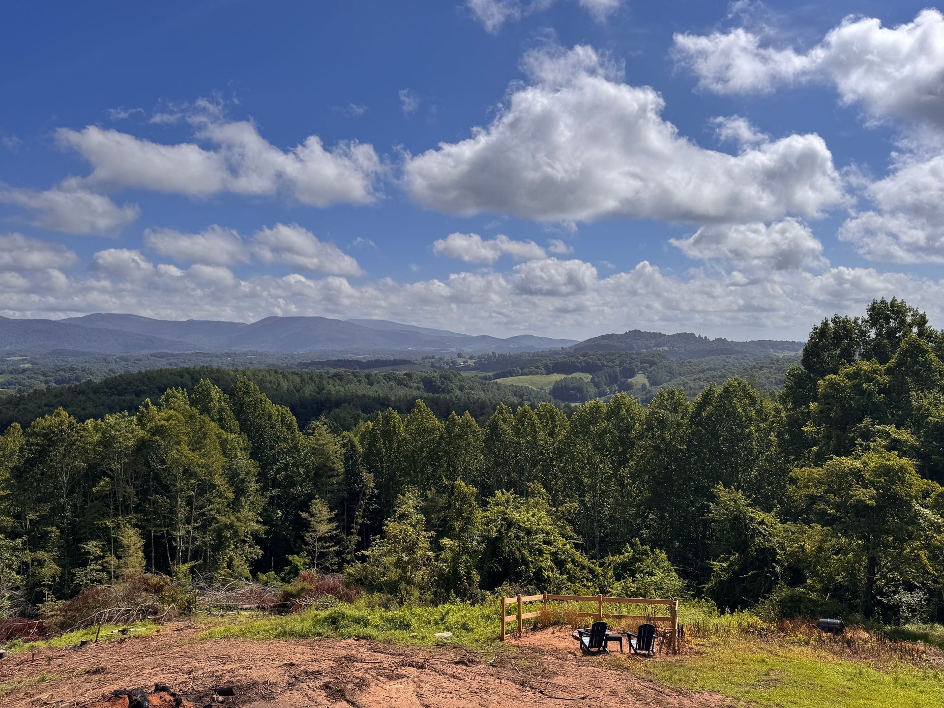 Sunny landscape with trees, distant hills, and a cloudy blue sky