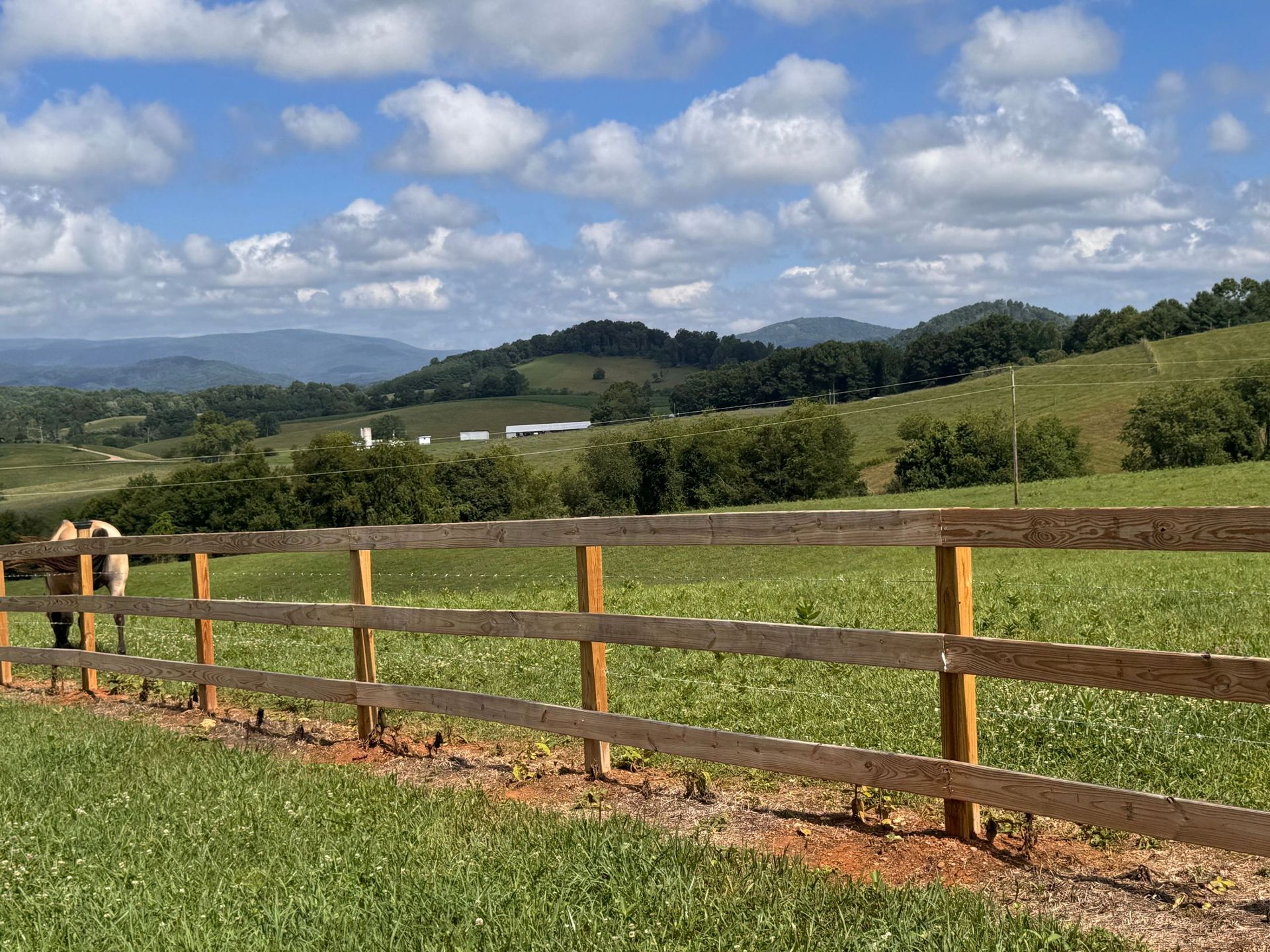 Wooden fence overlooking green fields and hills under a partly cloudy sky