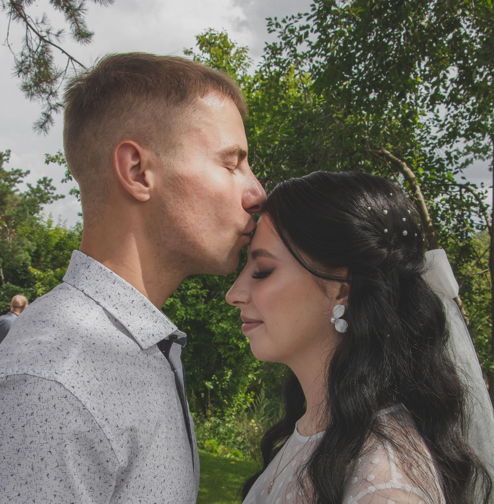 Couple outdoors, man kissing woman’s forehead under trees