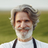 Smiling bearded person with gray hair in a white shirt standing in a grassy field