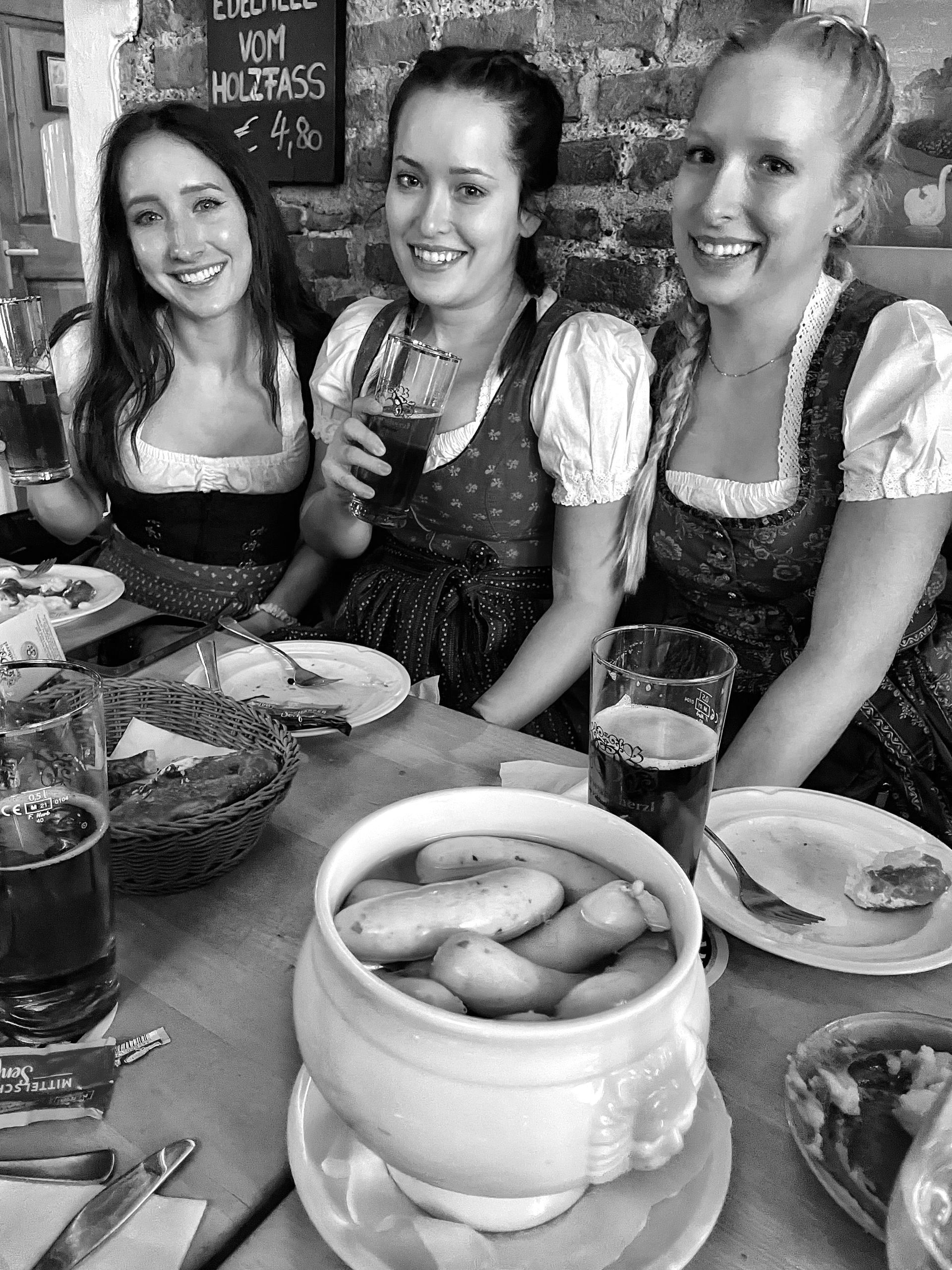 Three women are sitting at a table with plates of food and drinks.
