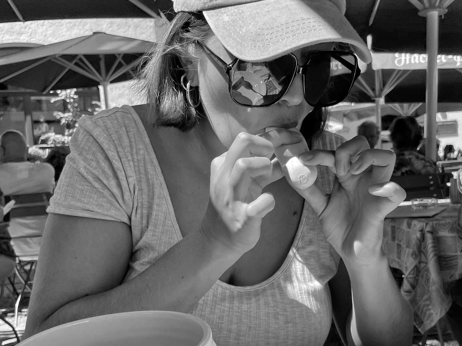 A woman wearing sunglasses and a hat is eating a piece of food.