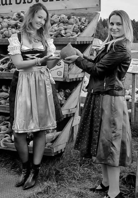Two women are standing next to each other in front of a fruit stand.