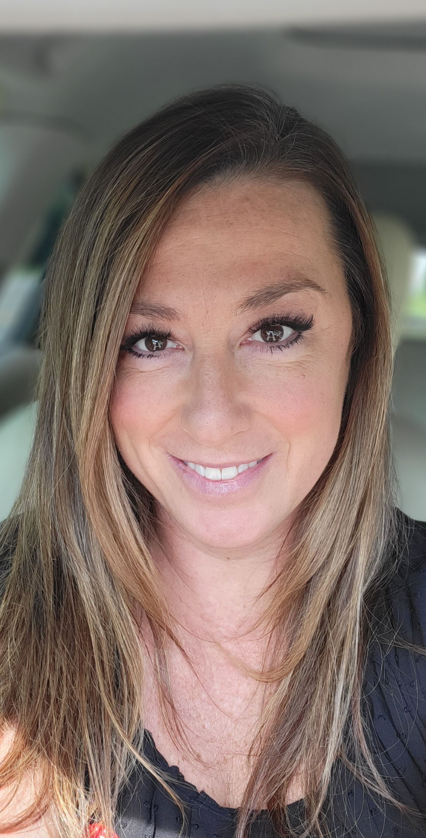 A woman with long hair is smiling for the camera while sitting in a car.