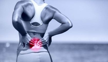 A woman is holding her back in pain while standing on the beach.