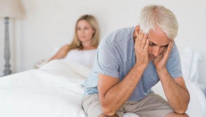 A man is sitting on a bed with his head in his hands.