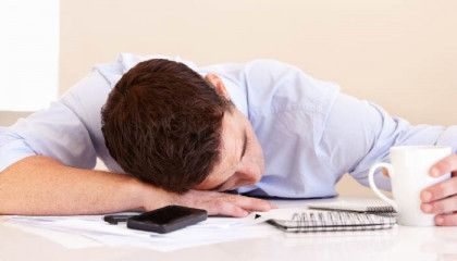 A man is sleeping at a desk with a cup of coffee.