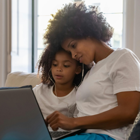 Mother and child using a laptop on a couch in a bright living room