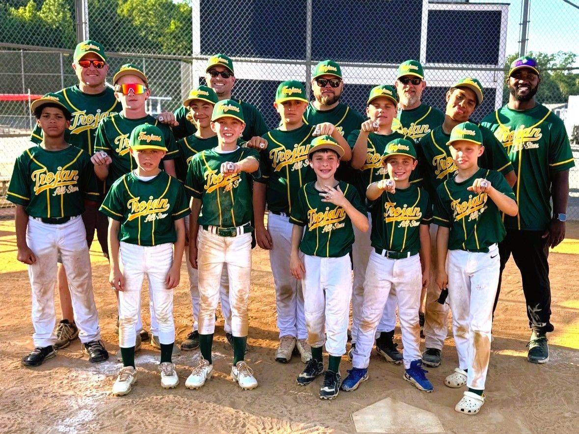 Youth baseball team posing in green jerseys and white pants on a field, with coaches standing behind them.