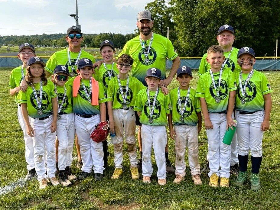 Youth baseball team in green jerseys posing with trophies on a field after a championship game