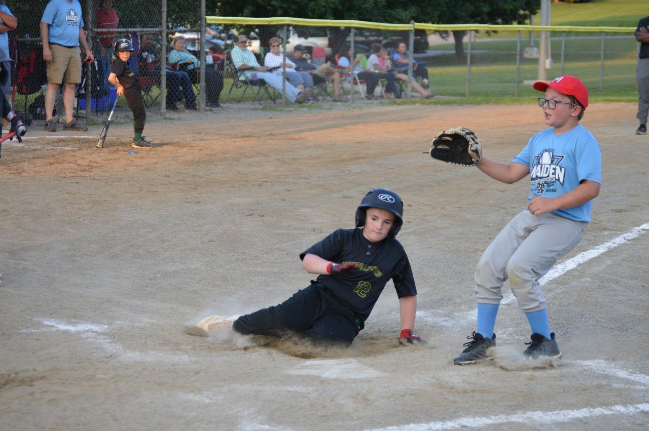 Youth baseball player slides into home plate as catcher reaches with glove nearby.