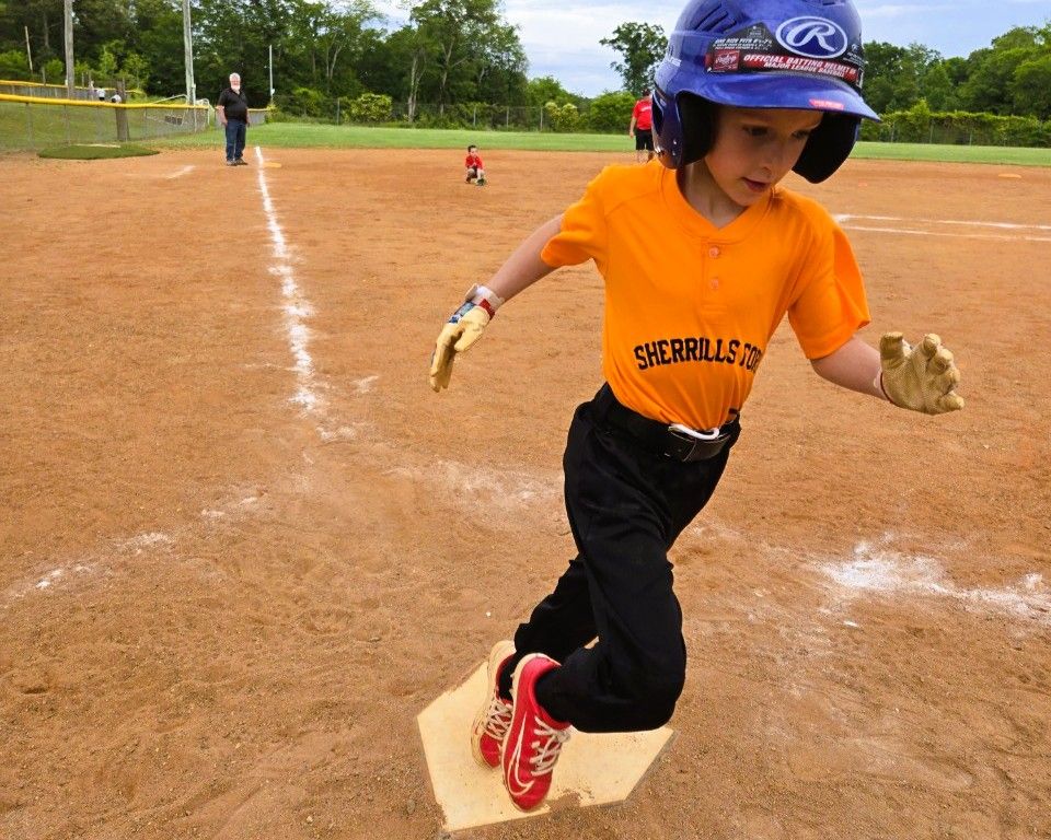 Boy in orange shirt and helmet running toward home base during a baseball game.