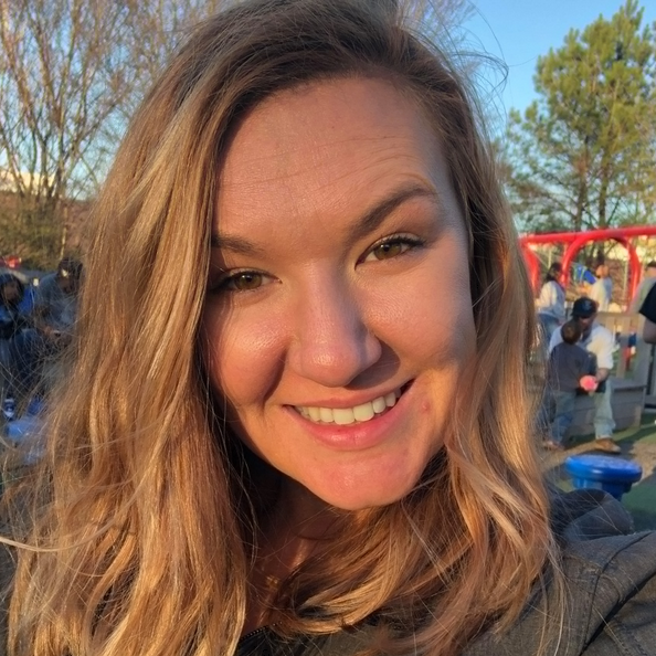 Woman smiling outdoors at a playground. Golden sunlight. People in background.