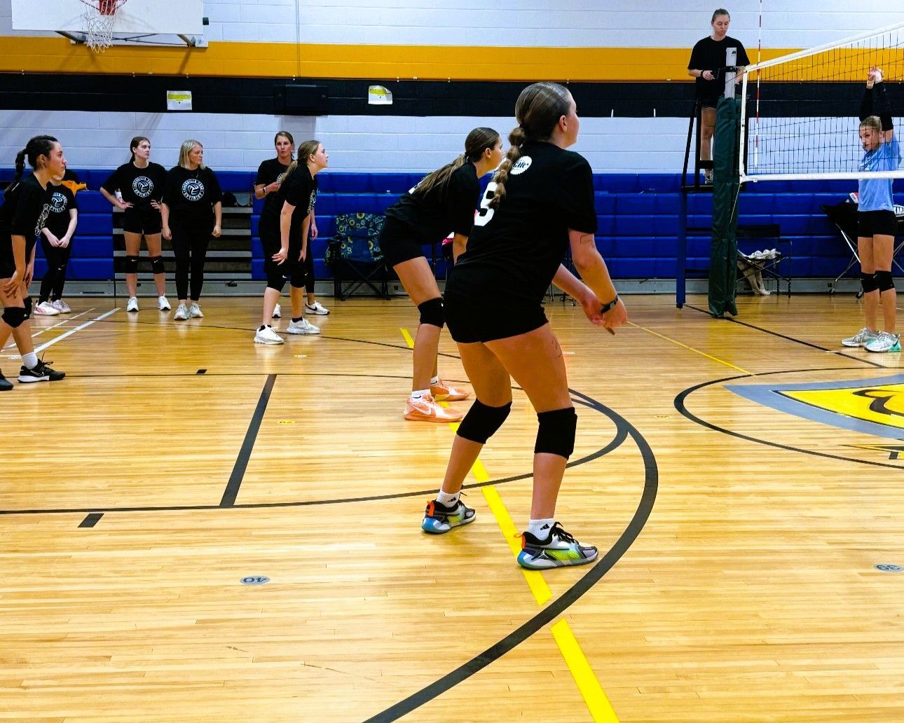 Volleyball players in black jerseys practice on an indoor gym court