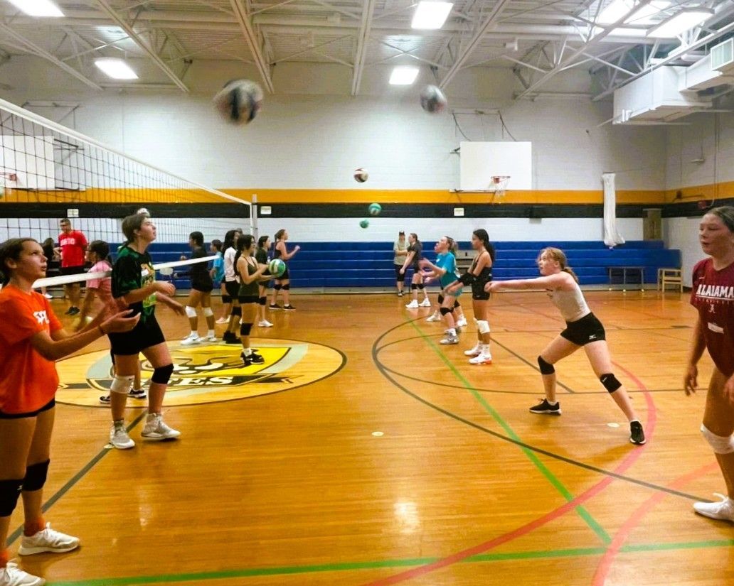Volleyball players practicing in a gymnasium. Players volley a ball over a net.
