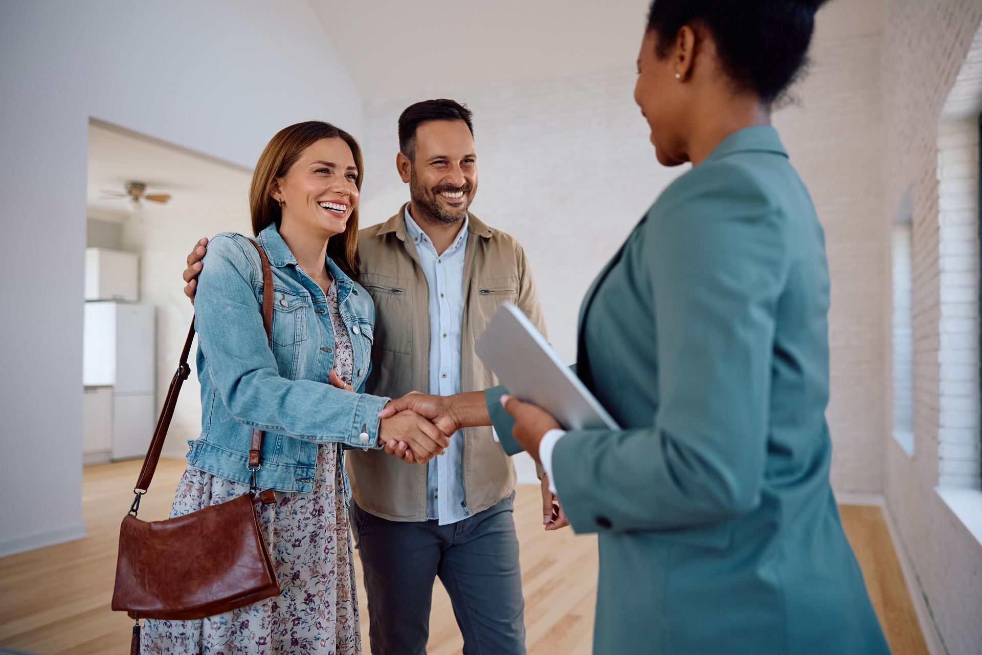 A woman is shaking hands with a man and woman in an empty room.